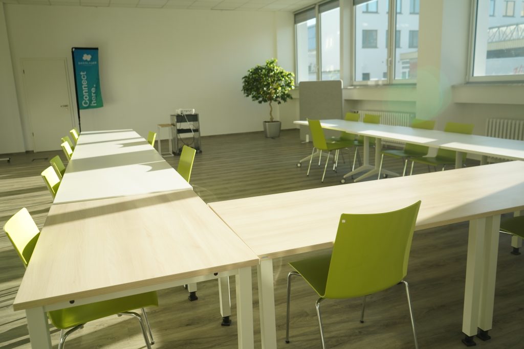 Ein Meetingraum mit Tischen in U-Form, einer hellen Fensterfront und Pflanzen